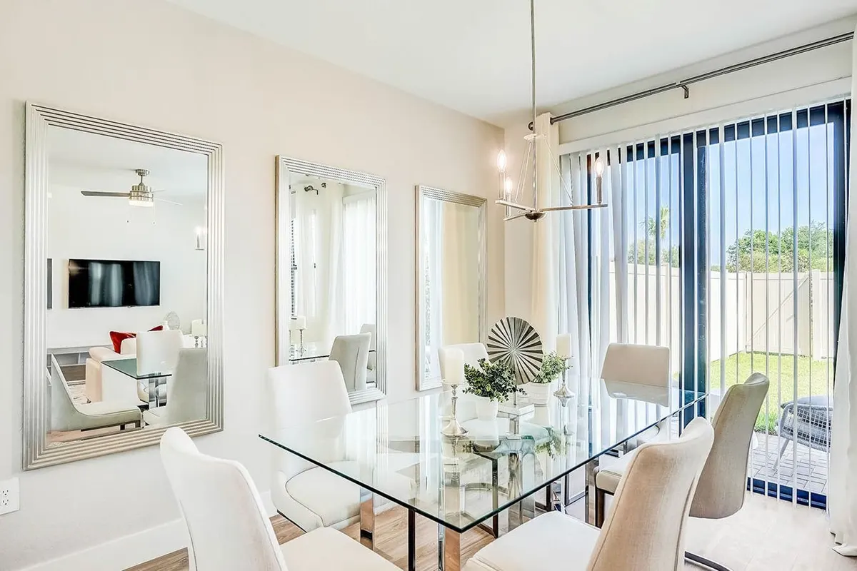 Dining area with a glass table and tall mirrors beside sliders to the yard