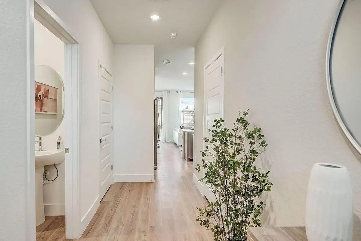 Entry hall with a round mirror and a tall plant, past the powder room door
