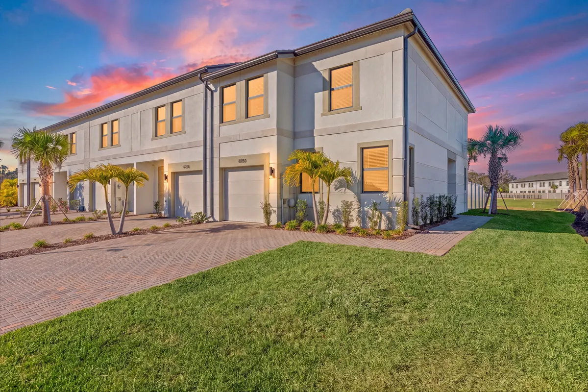 Row of Opal townhomes at dusk with lit windows, single-car garages and a green front lawn