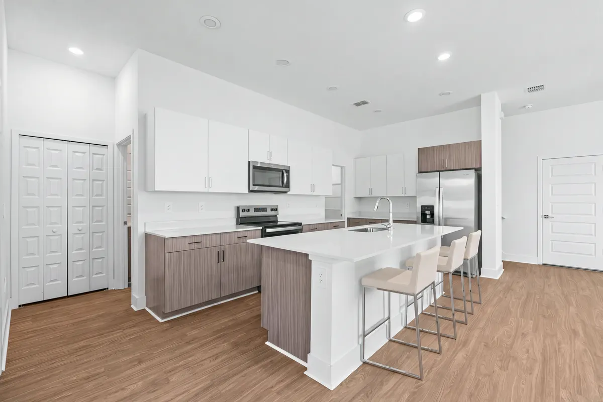 Cypress kitchen with three stools at the white island, wood and white cabinets and stainless appliances. Virtually staged.