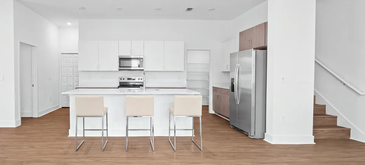 Cypress kitchen island with three ivory and chrome stools, stainless appliances and the staircase to the right. Virtually staged.