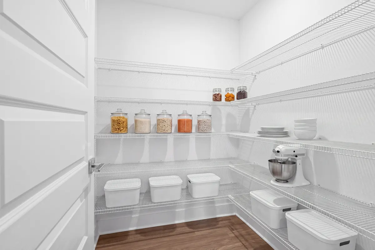 Cypress walk-in pantry with white wire shelving on two walls, glass canisters of pasta, rice, oats, lentils and beans, white plates and bowls, a stand mixer and lidded white bins. Virtually staged.