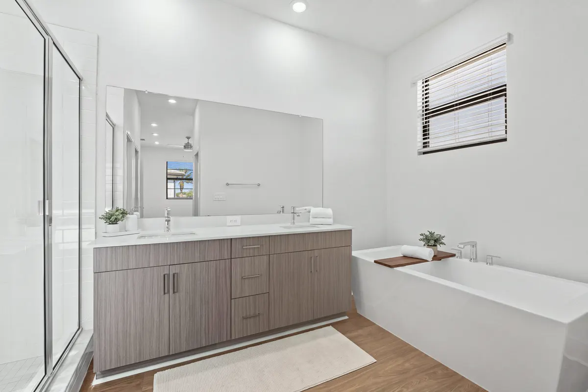 Cypress primary bathroom with a glass shower, a double vanity with a soap tray and folded towels, a bath mat, and a wooden bath tray across the freestanding tub. Virtually staged.