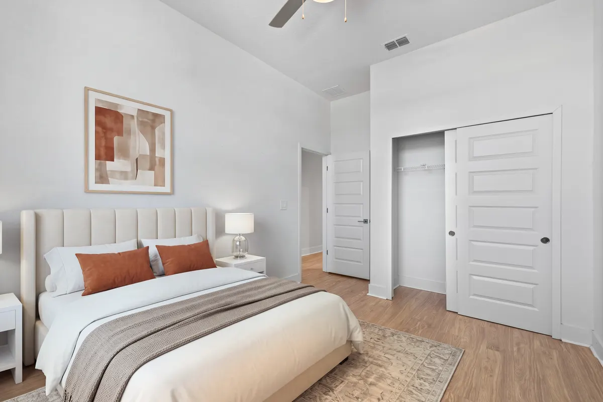 Maple bedroom with an upholstered bed, two nightstands, abstract art and a rug beside a sliding-door closet. Virtually staged.