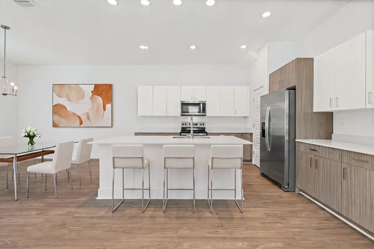 Maple kitchen with a white island, three stools and a dining table beside it. Virtually staged.