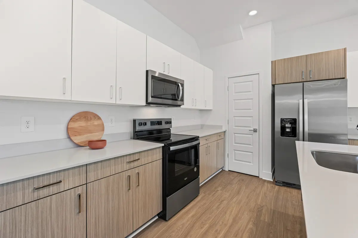 Maple kitchen with a round oak cutting board and a small terracotta bowl on the counter beside the range. Virtually staged.