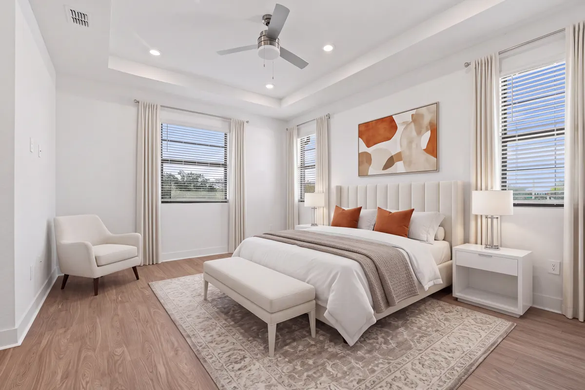 Maple primary bedroom with an upholstered bed, two nightstands, a bench, an armchair and a rug under a tray ceiling. Virtually staged.